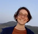 Patrícia's photo, grinning joyfully with a mountain behind.
